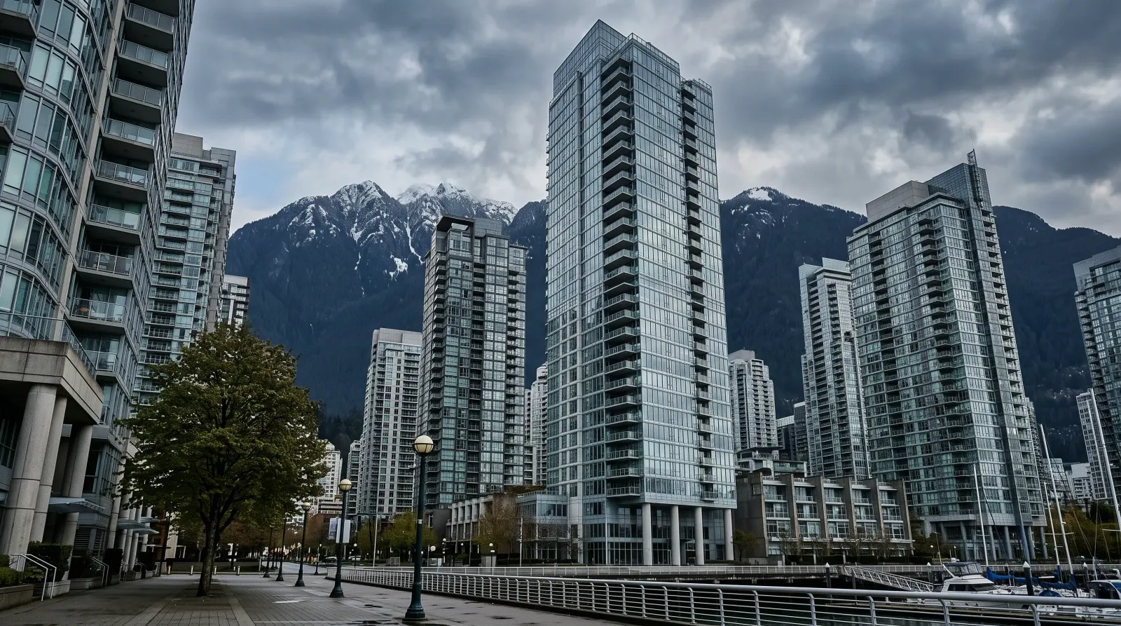 Modern Vancouver condominium towers in Coal Harbour with snow-capped North Shore mountains backdrop, overcast Pacific Northwest sky