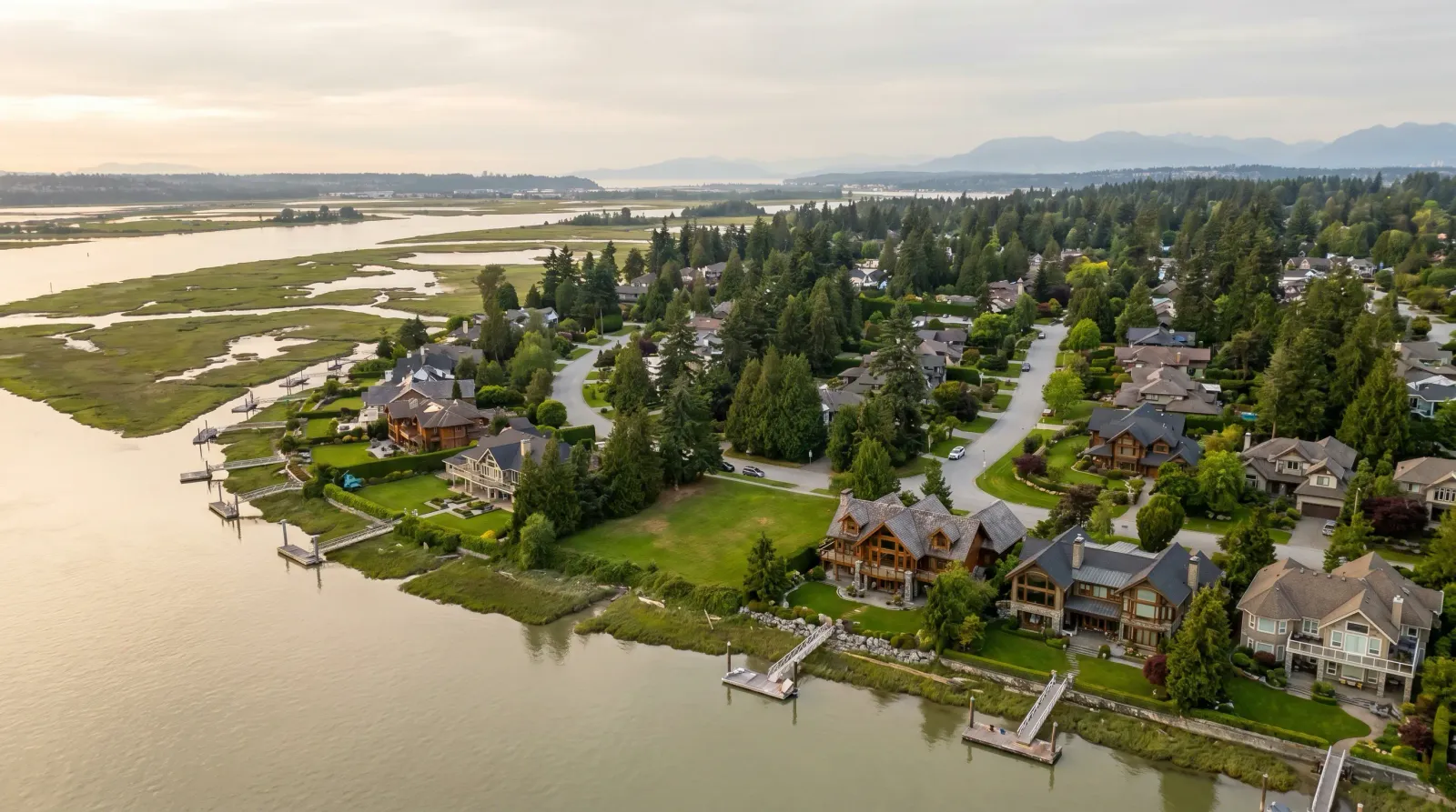 Aerial view of waterfront homes on large lots along the Fraser River estuary in Richmond, BC, with North Shore mountains in the distance