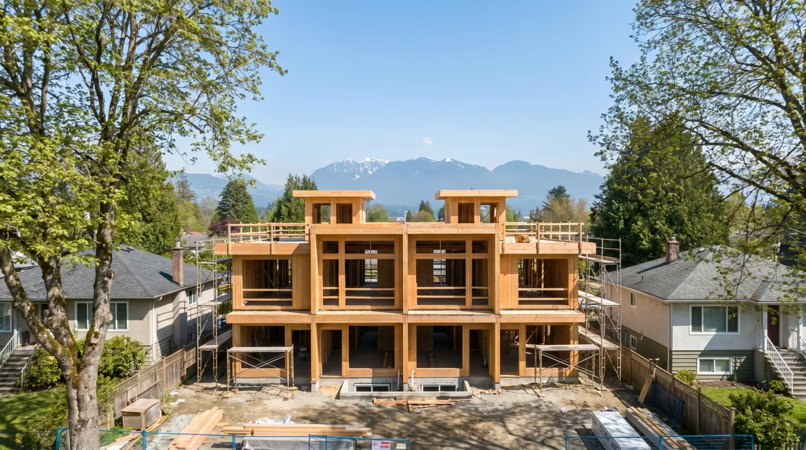 Vancouver multiplex under construction with exposed wood-frame structure, scaffolding, and North Shore mountains in background