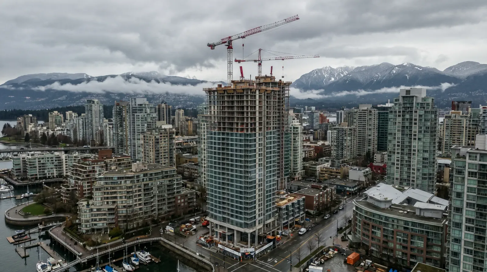 Aerial view of partially constructed Vancouver presale condo tower with construction cranes against North Shore mountains under overcast sky