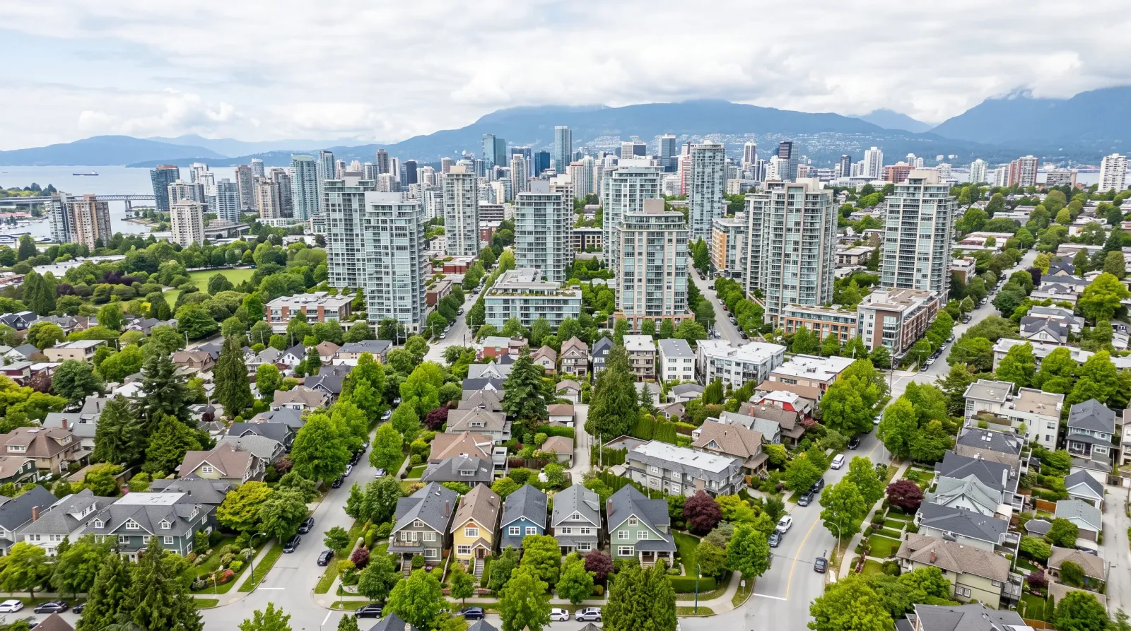 Aerial view of Vancouver neighbourhoods showing mix of detached homes and condo towers with North Shore mountains in background